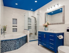 A dark blue and white bathroom with accent tiles on the bathtub and a dark blue ceiling and sink.
