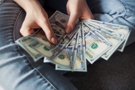 A person holding a few 100-dollar bills while sitting cross-legged on the floor